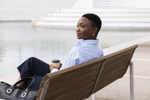 Smiling businesswoman sitting with coffee cup on bench - JPTF01297