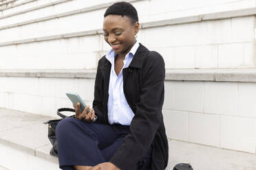 Happy businesswoman using smart phone on stairs - JPTF01300