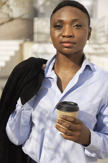 Businesswoman standing with coffee cup on sunny day - JPTF01301
