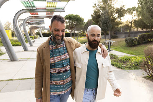 Gay couple walking with arm around in park at sunset - JPTF01302