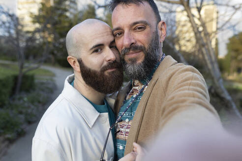 Smiling gay couple taking selfie in park at sunset - JPTF01306