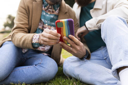 Gay couple using mobile phone in park - JPTF01311