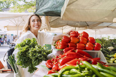 Happy woman buying leafy vegetables and red bell pepper in farmer's market - NDEF00998
