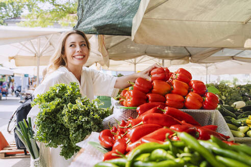 Glückliche Frau kauft Blattgemüse und rote Paprika auf dem Bauernmarkt - NDEF00998