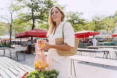 Smiling woman buying lemons in farmer's market on sunny day - NDEF01006