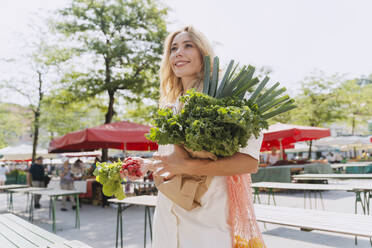 Happy woman holding fresh leafy vegetables in farmer's market - NDEF01008