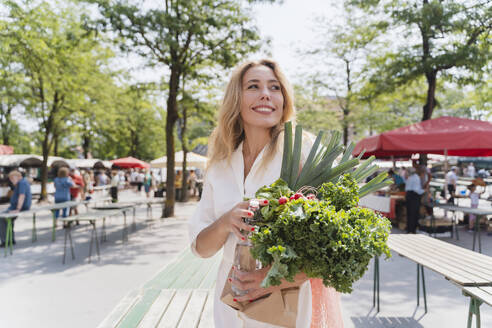 Glückliche Frau mit Gemüse auf einem Bauernmarkt an einem sonnigen Tag - NDEF01011