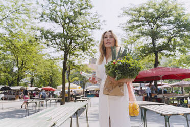 Smiling woman holding water bottle and groceries in farmer's market - NDEF01012