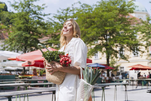 Glückliche Frau mit Tüten voller Lebensmittel auf dem Bauernmarkt an einem sonnigen Tag - NDEF01026