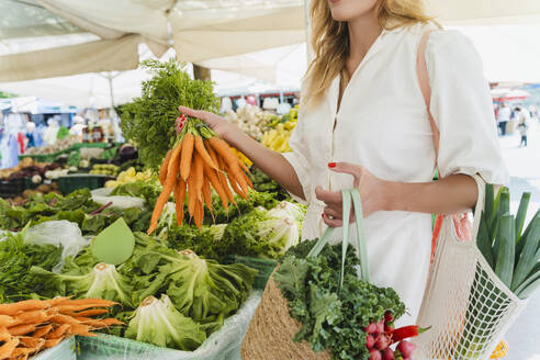 Frau kauft ein Bündel Karotten auf dem Markt - NDEF01029