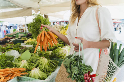 Woman buying bunch of carrots in market - NDEF01029