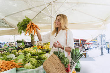 Glückliche Frau kauft ein Bündel Karotten auf dem Markt - NDEF01031