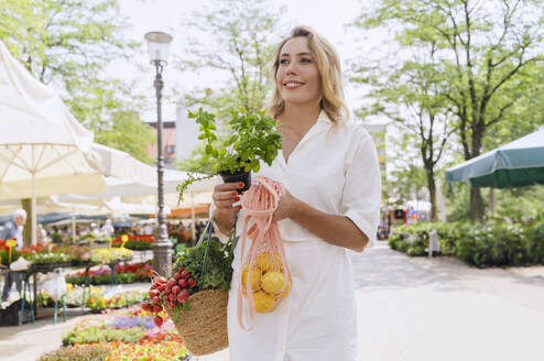 Glückliche Frau mit Minzsämling und Lebensmitteln auf dem Markt - NDEF01046