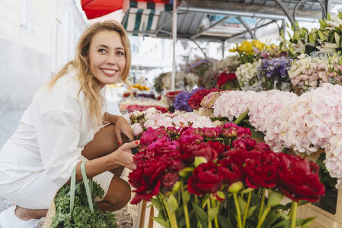 Glückliche blonde Frau kauft Blumen auf dem Markt - NDEF01049