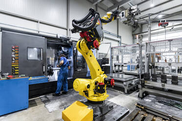 Technician operating cnc machinery behind yellow robotic arm - AAZF00933