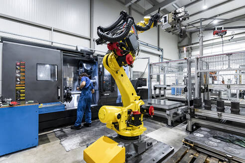 Technician operating cnc machinery behind yellow robotic arm - AAZF00933
