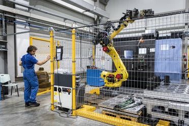 Technician examining robotic arm and machinery in factory - AAZF00945