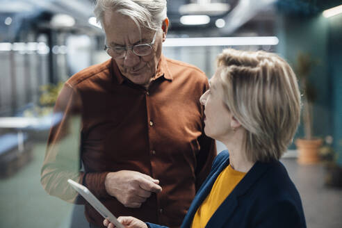 Businesswoman holding tablet PC discussing with colleague at work place - JOSEF20884