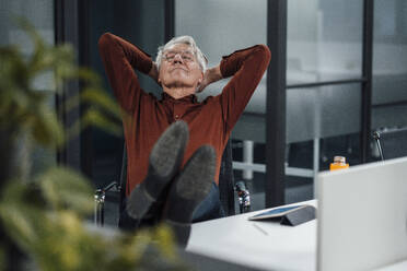 Senior businessman with hands behind head relaxing at desk in office - JOSEF20887