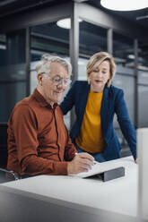 Senior businessman using tablet PC and discussing with colleague at desk in office - JOSEF20893