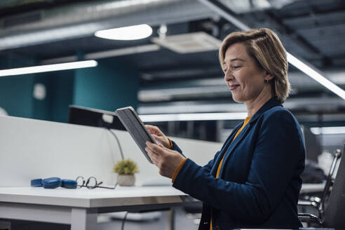 Lächelnde Geschäftsfrau, die ihre Strategie auf einem Tablet-PC am Arbeitsplatz plant - JOSEF20900