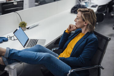 Geschäftsfrau mit Hand am Kinn, die auf einen Laptop im Büro schaut - JOSEF20901