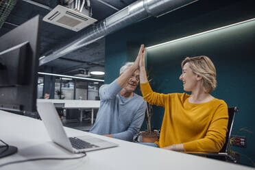 Business colleagues giving high-five to each other at desk in office - JOSEF20915