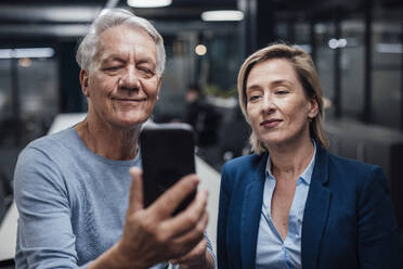 Smiling businesswoman sharing smart phone with colleague at work place - JOSEF20924