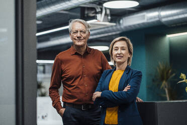 Smiling businesswoman and businessman in illuminated office - JOSEF20937