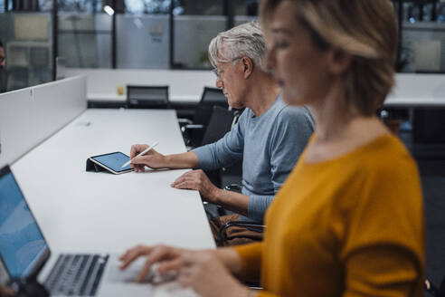 Älterer Geschäftsmann arbeitet am Tablet-PC eines Kollegen am Schreibtisch im Büro - JOSEF20951