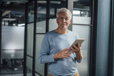 Smiling senior businessman holding tablet PC at work place - JOSEF20962