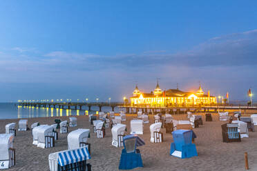 Deutschland, Mecklenburg-Vorpommern, Ahlbeck, Strandkörbe mit Kapuze und beleuchtete Seebrücke in der Abenddämmerung - EGBF00891