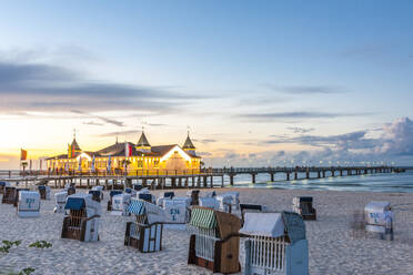 Germany, Mecklenburg-Vorpommern, Ahlbeck, Hooded beach chairs at sunset with pier and bathhouse in background - EGBF00898