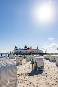 Deutschland, Mecklenburg-Vorpommern, Ahlbeck, Sonne scheint über Strandkörbe mit Kapuze und Badehaus im Hintergrund - EGBF00906