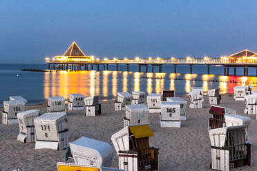 Germany, Mecklenburg-Vorpommern, Ahlbeck, Hooded beach chairs and illuminated pier at dusk - EGBF00911