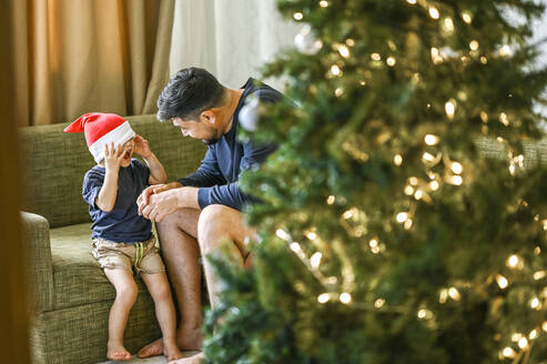 Vater und Sohn vergnügen sich auf dem Sofa neben dem Weihnachtsbaum - ANAF02085