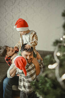 Lächelnder Vater und Söhne feiern Weihnachten zu Hause - ANAF02090
