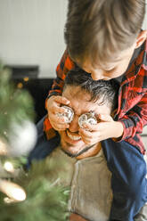 Son covering father's eyes with Christmas lights at home - ANAF02094