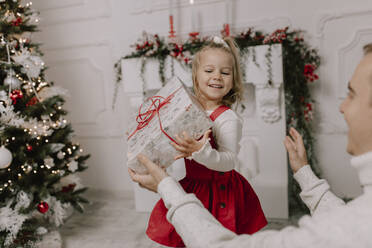 Glückliche Tochter hält Geschenk in der Nähe von Weihnachtsbaum - VIVF01067