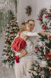 Lächelnder Vater, der seine Tochter trägt und den Weihnachtsbaum berührt - VIVF01069
