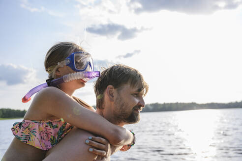 Vater nimmt seine Tochter in der Nähe des Sees huckepack - EYAF02794
