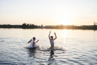 Bruder und Schwester spielen im See bei Sonnenuntergang - EYAF02799