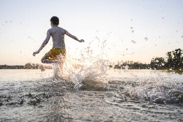 Unbekümmerter Junge läuft im See und spritzt Wasser - EYAF02801