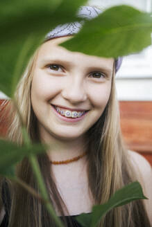 Smiling girl wearing dental braces near leaf - EYAF02803