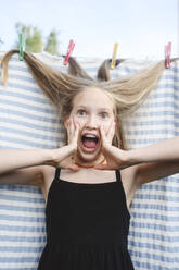 Überraschtes blondes Mädchen mit Haaren in Wäscheklammer - EYAF02804