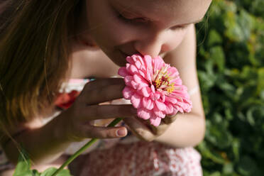 Girl holding and smelling pink flower in garden - EYAF02807