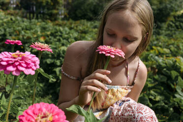 Blondes Mädchen riecht an rosa Blume im Garten - EYAF02808