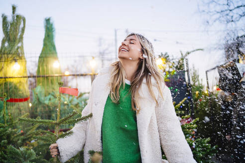 Smiling woman with eyes closed standing near Christmas tree at market - MDOF01462