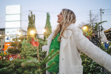 Blond woman standing with arms outstretched at Christmas market - MDOF01468