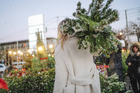 Blond woman carrying Christmas tree at market - MDOF01477